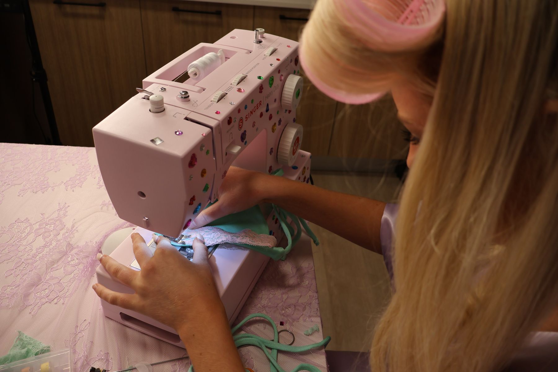 A woman in hair rollers sewing a mint bikini